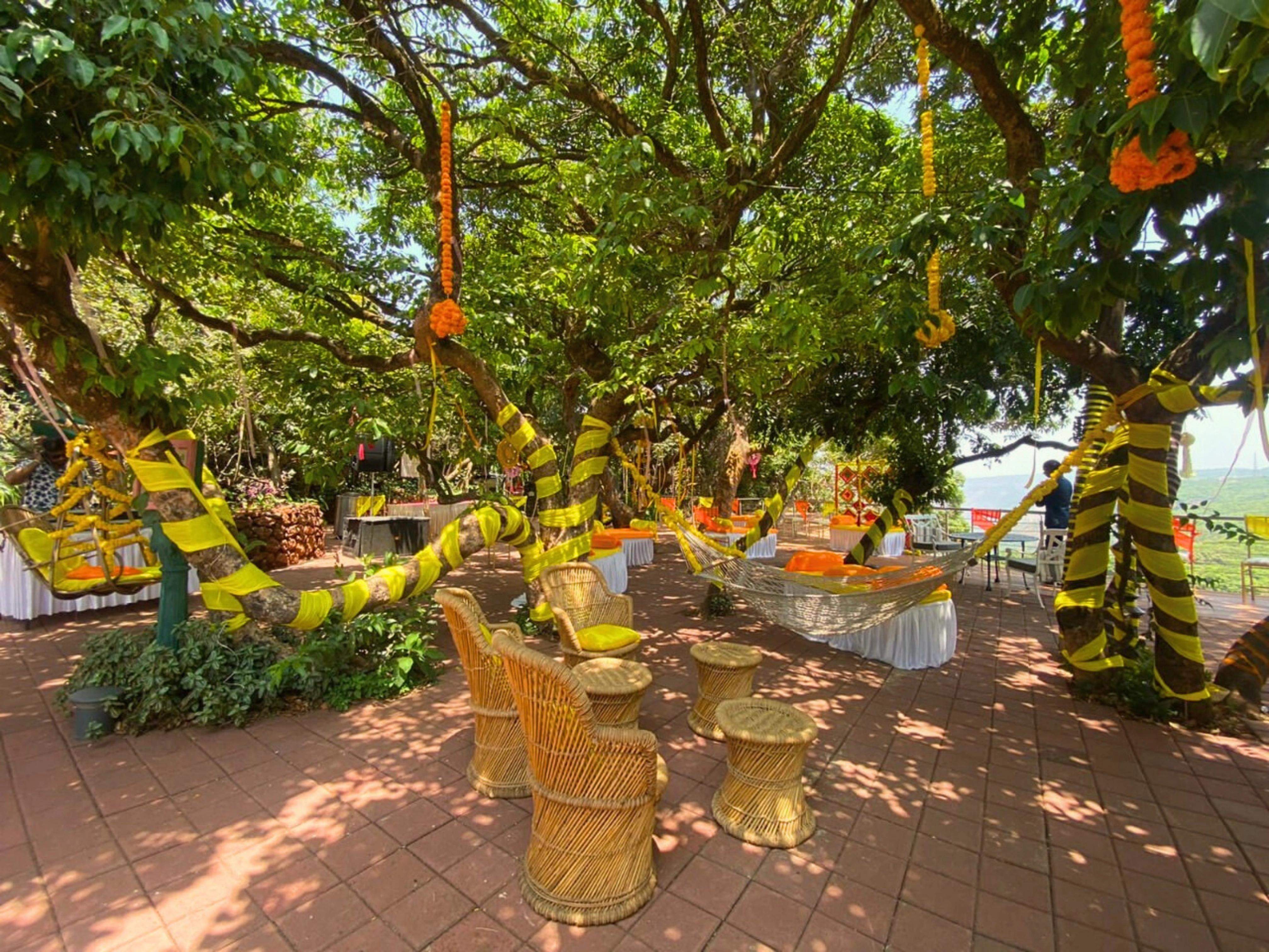 Outdoor dining under the forest canopy at Ramsukh Resort, Mahabaleshwar, with round tables and red chairs.